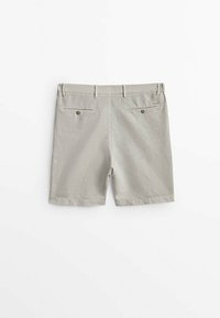 Short beige clair avec deux poches arrière à boutons et passants de ceinture, posé à plat sur une surface blanche.