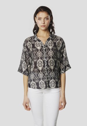 Camisa de manga corta en blanco y negro con estampado, cuello con solapa, corte holgado y cierre de botones. Combinada con pantalones blancos.