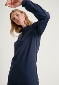 Navyblauwe top met lange mouwen, kraag en knoopsluiting. Zachte, rekbare stof met geribbelde manchetten en zoom.