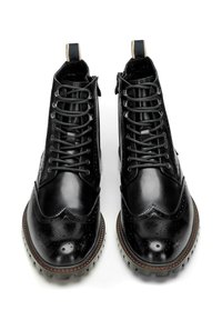 Botas de cuero negras hasta el tobillo con punteras redondas, acentos perforados, diseño de cordones y suelas de goma resistentes. Detalles de costura en contraste en color marrón claro.