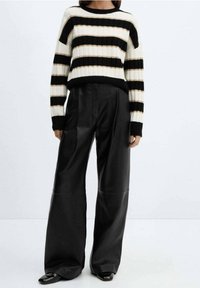 Sweter w czarno-białe paski z prążkowaną fakturą i okrągłym dekoltem, połączony z szerokimi czarnymi spodniami skórzanymi.