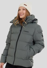 Puffi vihreä takki, jossa on vetoketjukiinnitys, iso huppu ja brodeerattu logo. Ominaisuuksiin kuuluvat joustavat hihansuut ja sivutaskut. Yhdistettynä kermaiseen beanie-hattuun.