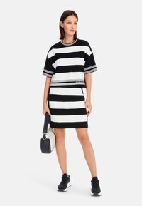 Black and white striped dress with a short sleeve top and a fitted skirt. Features a round neckline and logo accent on the hem. Black sneakers.