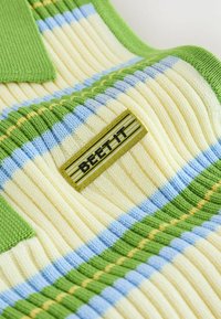 Tissu en maille côtelée avec des rayures vertes, jaunes et bleues, et une étiquette jaune avec un texte noir indiquant "BEEFY".