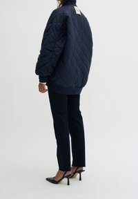 Námořnická prošívaná péřová bunda s žebrovanými manžetami, v kombinaci s tmavými džíny. Černé lodičky na zkušené s úzkou špičkou. Minimalistický design.