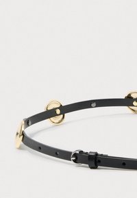 Cinto de couro preto com detalhes em metal dourado. Apresenta fivela ajustável e múltiplos furos para personalização do tamanho. Textura suave.