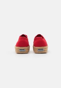 Red canvas shoes with a rounded shape and jute rope soles, featuring a logo on the heel and a smooth texture.