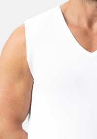 Witte mouwloze tanktop met V-hals, gemaakt van gestructureerde stof, met een aansluitend ontwerp dat de lichaamsvorm volgt.