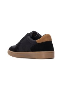 Zapatillas deportivas de ante y cuero negro con un refuerzo de ante marrón en el talón, suela de goma beige y puntera redonda. Cierre con cordones en la parte frontal.