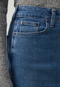 Jean en denim bleu foncé avec une taille haute, dotés de quincaillerie en métal, d'un design à cinq poches et d'une texture lisse.