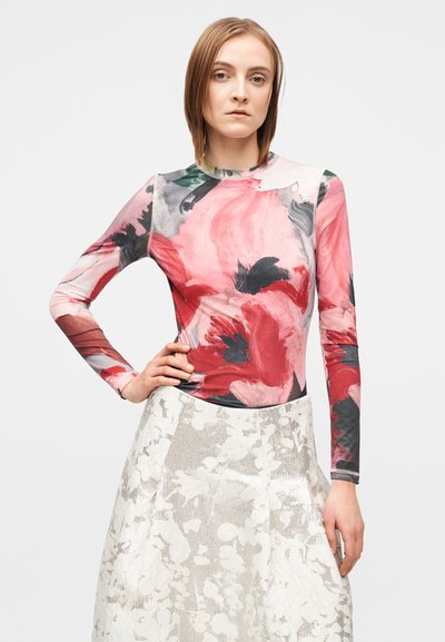 Μακρυμάνικη μπλούζα με ροζ και κόκκινο λουλουδένιο σχέδιο σε ελαφρύ ύφασμα, συνδυασμένη με ασημί υφασμάτινη φούστα με λουλουδένιο μοτίβο.