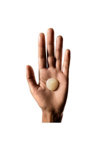 Hånd holder et glatt, sirkulært, gjennomsiktig kremfarget objekt. Hånden har middels brun hudtone, fingrene er spredd, håndflaten synlig.