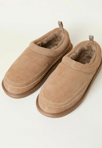 Beige suede slippers with soft fur lining, slip-on design, rounded toe, and a textured rubber sole for enhanced grip and comfort.