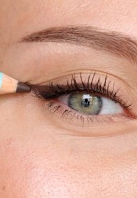 Una matita per eyeliner marrone è applicata vicino alla palpebra superiore, evidenziando lunghe ciglia scure e un'iride brillante e multicolore. Texture della pelle liscia visibile.