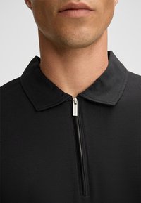 Czarny sweter z zamkiem i kołnierzykiem. Wykonany z gładkiej tkaniny, o minimalistycznym wzornictwie i subtelnych detalach przeszyć.