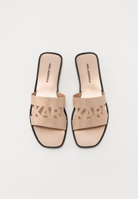 Sandales à glisser beiges avec de larges lanières présentant un logo "KARL" découpé, une doublure intérieure lisse et une semelle noire. Fini texturé sur les lanières.