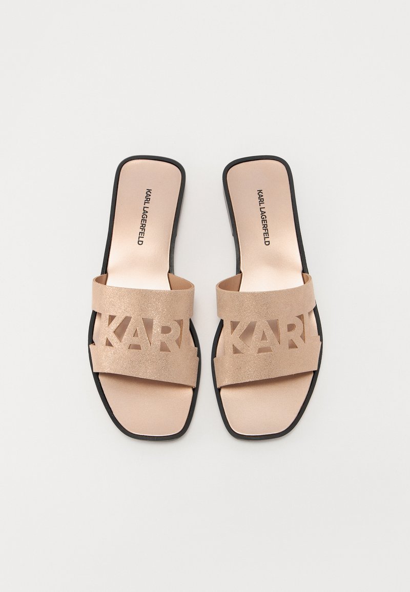 Sandales à glisser beiges avec de larges lanières présentant un logo "KARL" découpé, une doublure intérieure lisse et une semelle noire. Fini texturé sur les lanières.