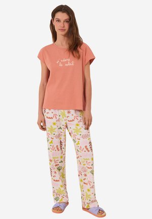 Geriefachtig roze katoenen T-shirt met de tekst "j'adore le soleil"; gecombineerd met gemusterde pastelkleurige pyjamabroek en lichtpaarse slippers.
