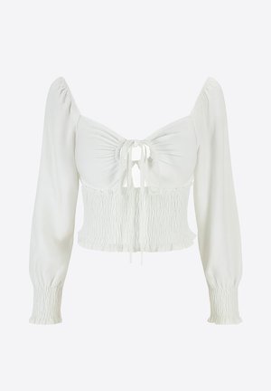 Hvid croppet top med lange pufærmer, der har en smocket krop og bindedetalje foran. Glat stof med en blød tekstur.
