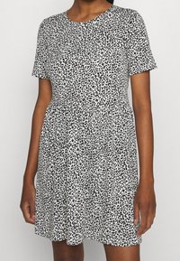 Robe à manches courtes blanche avec un motif léopard noir. Elle possède une taille cintrée et une jupe évasée. Confectionnée dans un tissu léger.