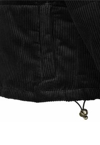 Gros plan sur un tissu en velours côtelé noir avec des rainures verticales, une poche zippée et un cordon ajustable avec des butées métalliques à l’ourlet.