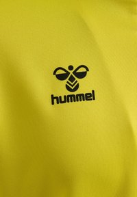 Gult tekstil med en sort logo af en stiliseret bi med mærkenavnet "hummel" under, på en glat, mat overflade.