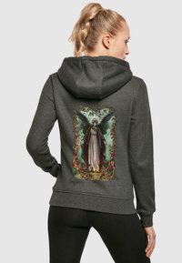 Grå hoodie med en detaljerad grafik av en ängel med vingar, omgiven av vinrankor och blommor på baksidan. Mjuk tygkvalitet, avslappnad passform.