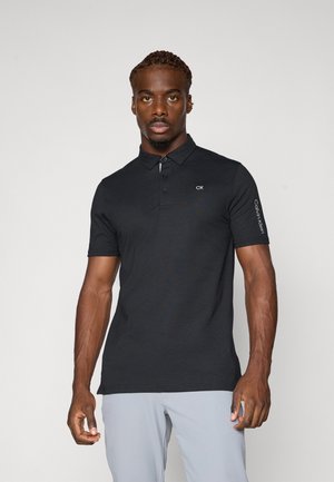Svart polo-skjorte med klassisk krage, korte ermer, tre-knappers placket, og "CK"-logo på brystet. Glatt tekstur.