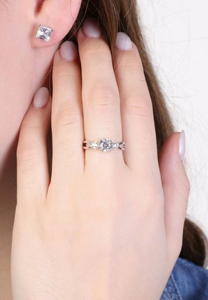 Sterling silver ring with a central clear gemstone and two smaller side stones. Square-shaped stud earrings with clear gemstones.