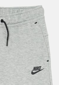 Szürke sportos joggerek, elasztikus derékpánttal, fekete zsinórral, oldalsó zsebekkel és fekete Nike logóval a bal alsó lábszáron.