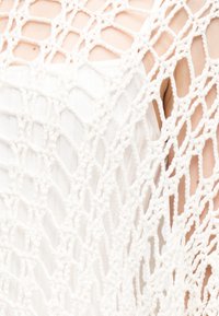 Λευκό κρίκετ τοπ με ανοιχτό, δίχτυ μοτίβο. Μαλακή υφή, στρωματοποιημένος σχεδιασμός που αποκαλύπτει το δέρμα από κάτω. Απλό και ελαφρύ.