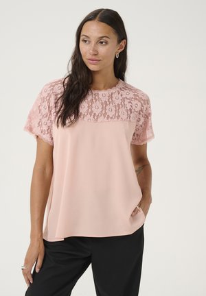 Lyserød bluse med en blondeoverlag ved skuldrene og korte ærmer, der har en glat tekstur og en afslappet pasform.