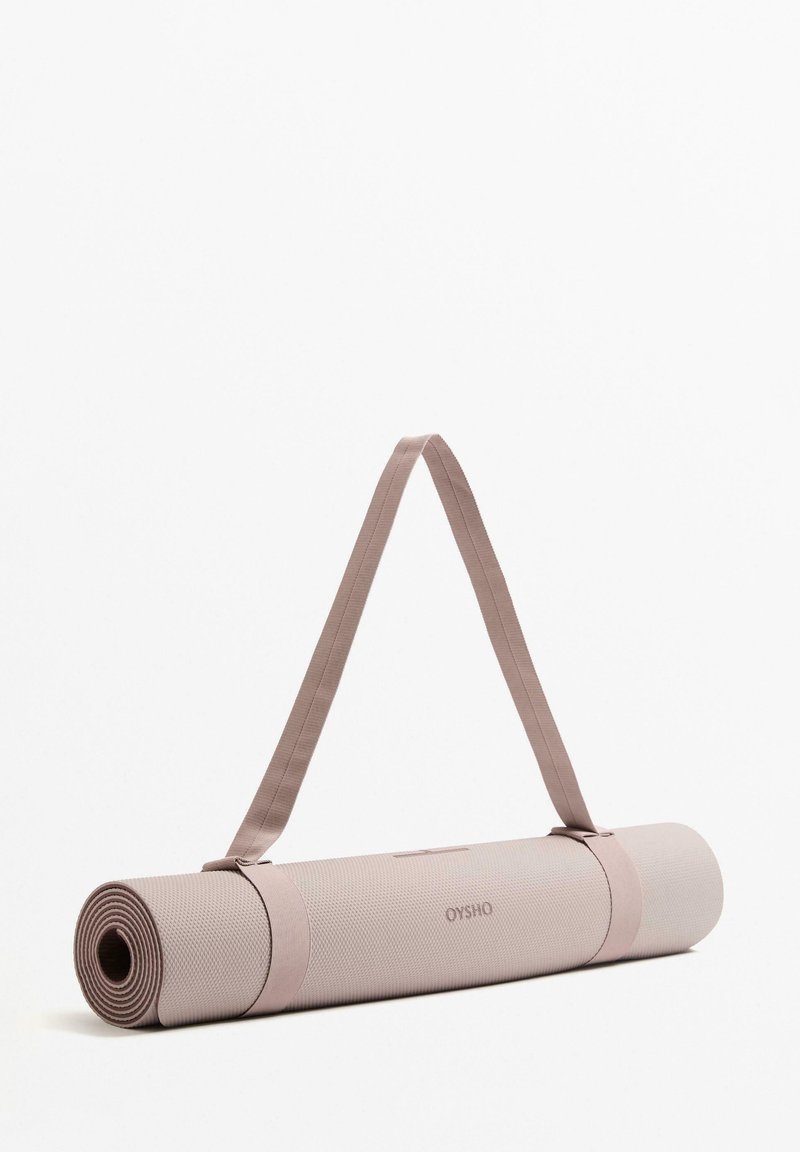 Barack rózsaszín jóga matrac texturált felülettel, összegöngyölve és azonos színű pánttal rögzítve, amelyen jól láthatóan az "OYSHO" márkanév szerepel.