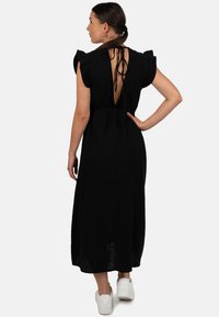 Zwarte maxi-jurk met ruches mouwen, open rug die wordt vastgemaakt met strikken, gemêleerde stof en een relaxte pasvorm. Geshikt met witte sneakers.