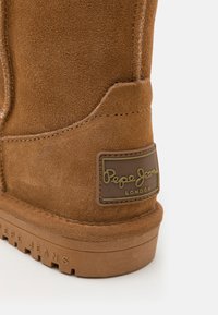 Botín de ante marrón con un acabado texturizado, que presenta una suela de goma y un parche de marca con el texto "Pepe Jeans London" en dorado.