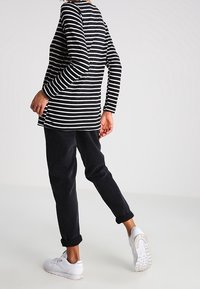 Black and white striped long-sleeve top with a relaxed fit, paired with dark pants and white sneakers. Smooth fabric with rolled cuffs.