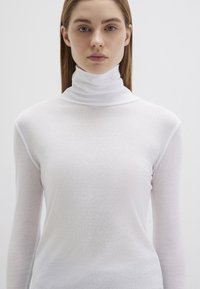 Weißes langärmliges Rollkragenoberteil aus leichtem, strukturiertem Stoff. Verfügt über einen hohen Kragen und nahtlose Schultern.