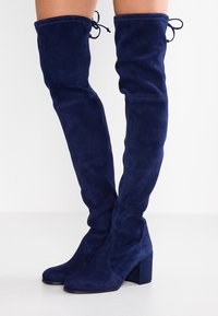 Marineblaue Wildleder-Stiefel über dem Knie mit Blockabsatz, die eine glatte Textur und eine Schleifenverzierung am oberen Ende aufweisen.