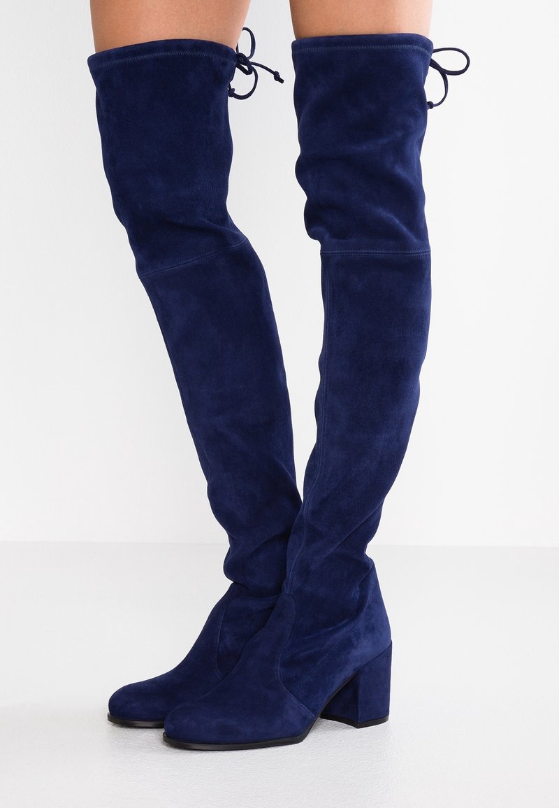 Marineblaue Wildleder-Stiefel über dem Knie mit Blockabsatz, die eine glatte Textur und eine Schleifenverzierung am oberen Ende aufweisen.