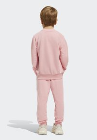 Ružový sveter a zodpovedajúce nohavice vyrobené z mäkkého materiálu, s bielymi bočnými pruhmi, vo voľnom strihu a s rebrovanými manžetami.