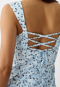 Modrá květinová šaty s křížovými ramínky na zadní straně a jemným stažením na šňúrku. Tkanina má texturovaný povrch.