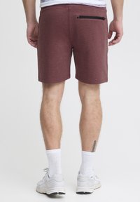 Shorts bordeaux en tissu texturé et doux. Équipés d'une poche arrière zippée. Coupés au-dessus du genou avec une taille élastique.