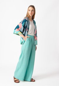 Žydrų, rožinių ir žalių gėlių raštų lengvas kimono, derinamas su laisvomis, šviesiomis turkio spalvos kelnėmis ir rudais sandalais.