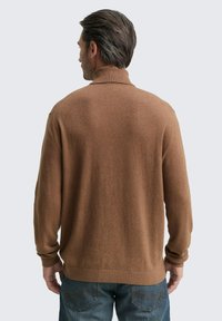 Brauner Strickpullover mit hohem Kragen, gerippten Bündchen und Saum, von hinten gezeigt. Die strukturierte Stoffqualität ergänzt die lässigen Denim-Hosen.