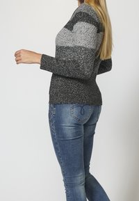 Sweter dziany w szare i czarne paski, z długimi rękawami; zestawiony z niebieskimi dżinsami, które mają kwiatowe hafty na tylnych kieszeniach.