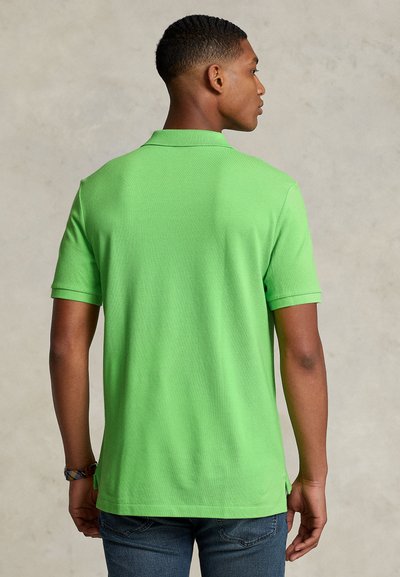 Polo verde com mangas curtas, apresentando um tecido de malha texturizada. Inclui uma gola clássica e uma bainha reta com fendas laterais.