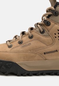 Stivale da trekking in suede tan con accenti in rete, dettagli neri e suola in gomma testurizzata caratterizzata da un motivo a battistrada robusto. Marchio Timberland in evidenza.