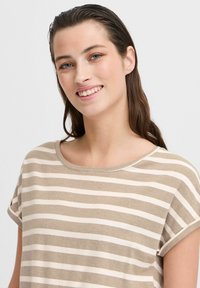 T-shirt rayé en beige et blanc. Matière en coton douce, col rond, manches courtes retroussées, avec des rayures horizontales et une coupe décontractée.