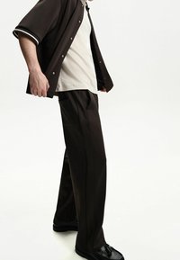 Dark brown, short-sleeve shirt with white accents, paired with matching brown pants featuring side pockets and a straight-leg fit; black shoes.