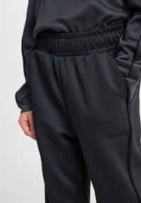 Svarta atletiska byxor med texturerad tyg, med resårmidja och sidofickor. Inkluderar en diskret logotyp på den nedre delen av benet.